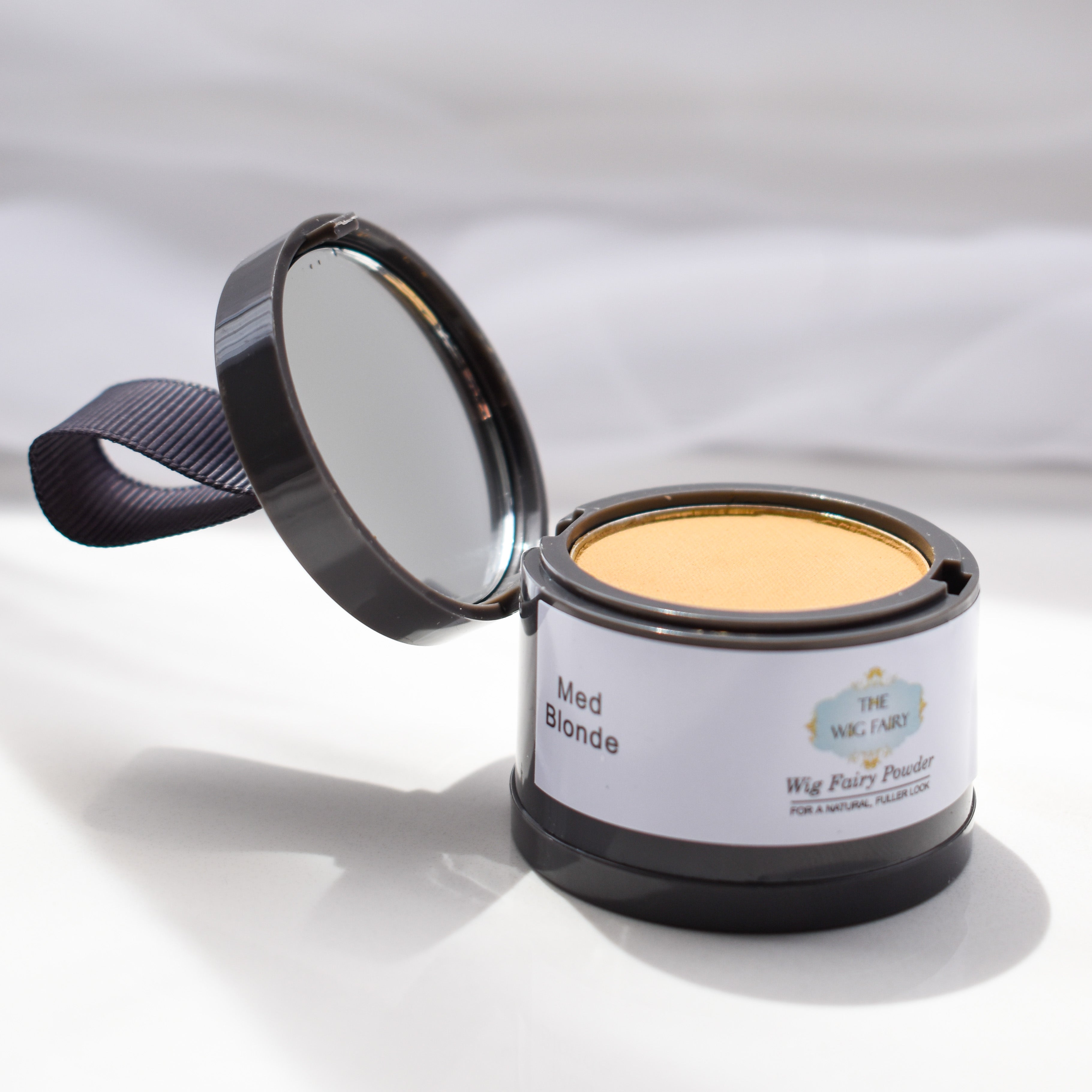 Compact of medium blonde Wig Fairy Powder opened to reveal product and mirror, displayed on a white surface.