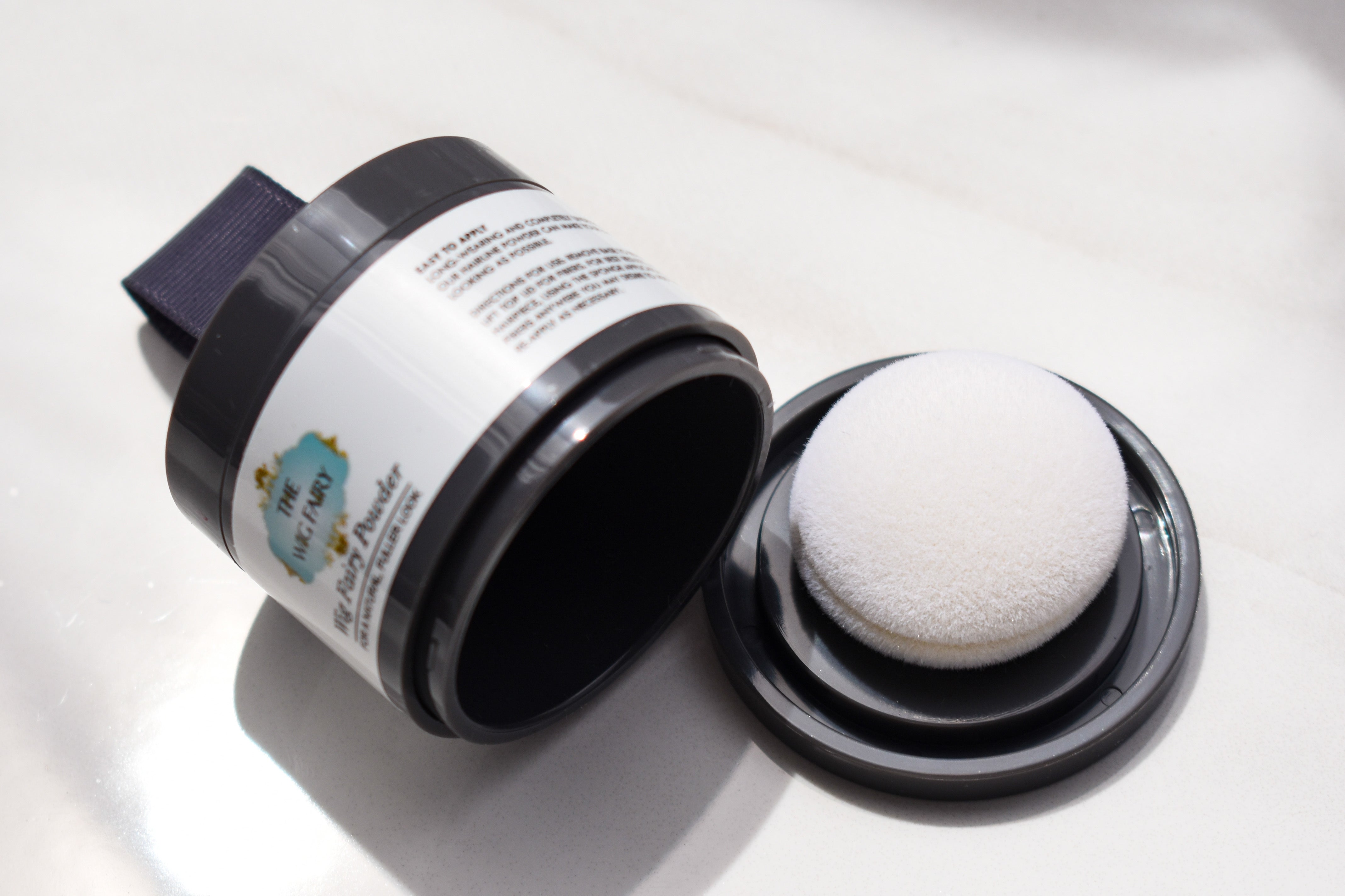 Open container of The Wig Fairy Powder in medium blonde with puff applicator lid shown beside it.