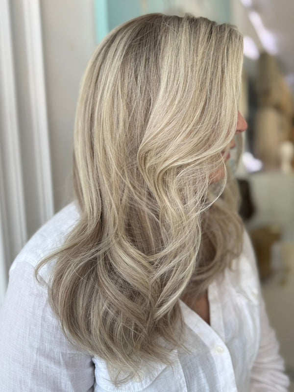 Side profile of model wearing a long, cool ash blonde lace wig styled with soft waves and natural dimension.