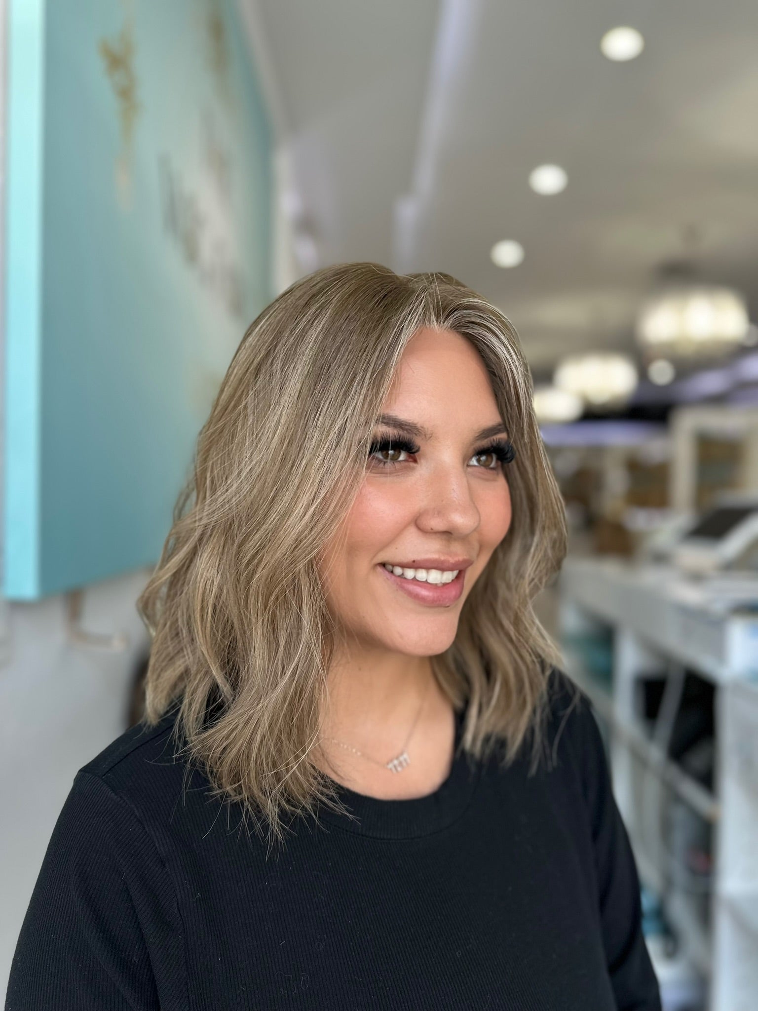Smiling model wearing the Margot wig, highlighting the natural blend of cool blonde shades and effortless wave pattern.