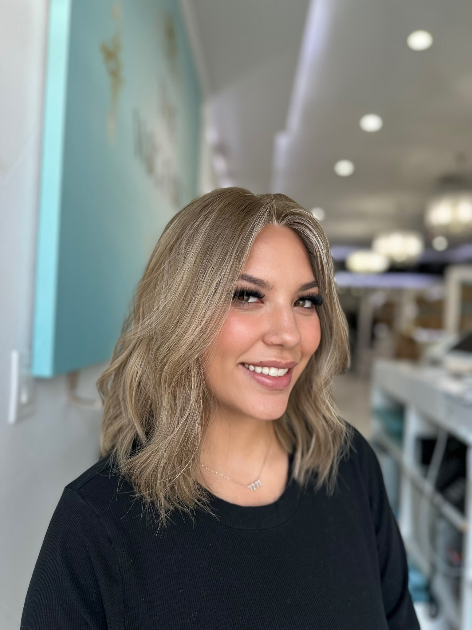 Model wearing the Margot wig in a center part, styled with natural waves and a sandy blonde tone with ash lowlights.