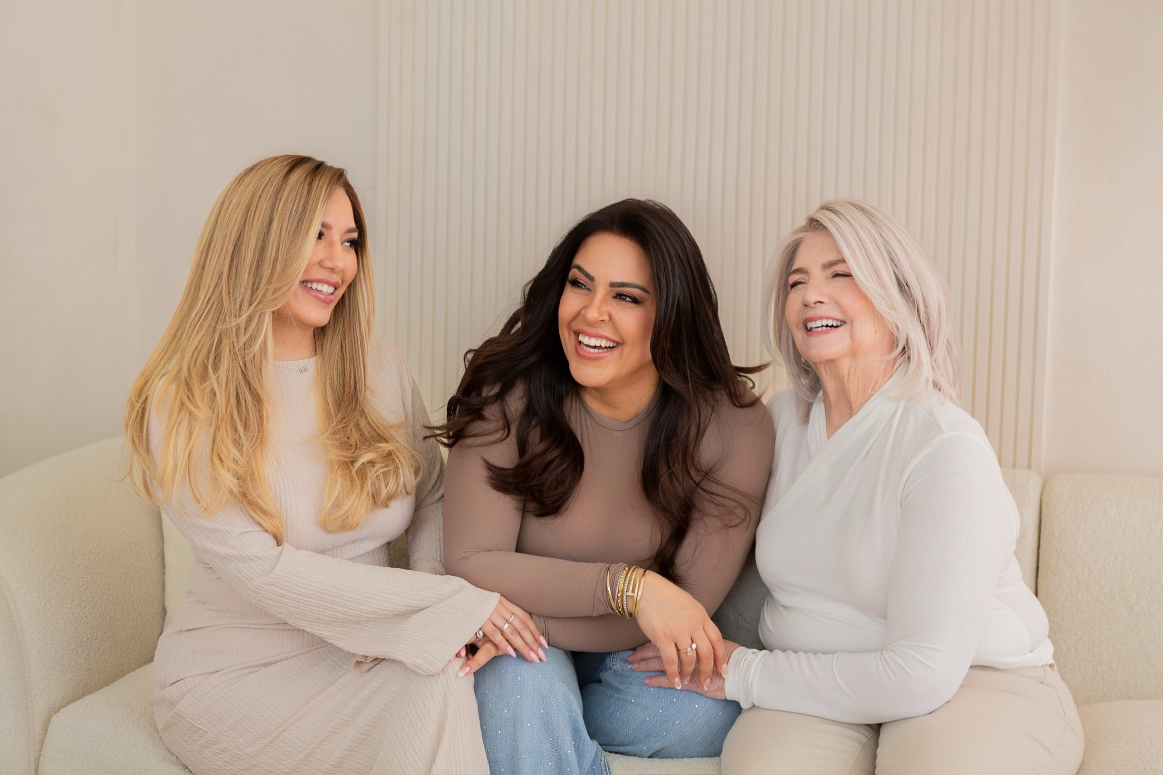 Three women wearing blonde, brunette, and grey human hair wigs smiling together on a beige couch – Wig Fairy