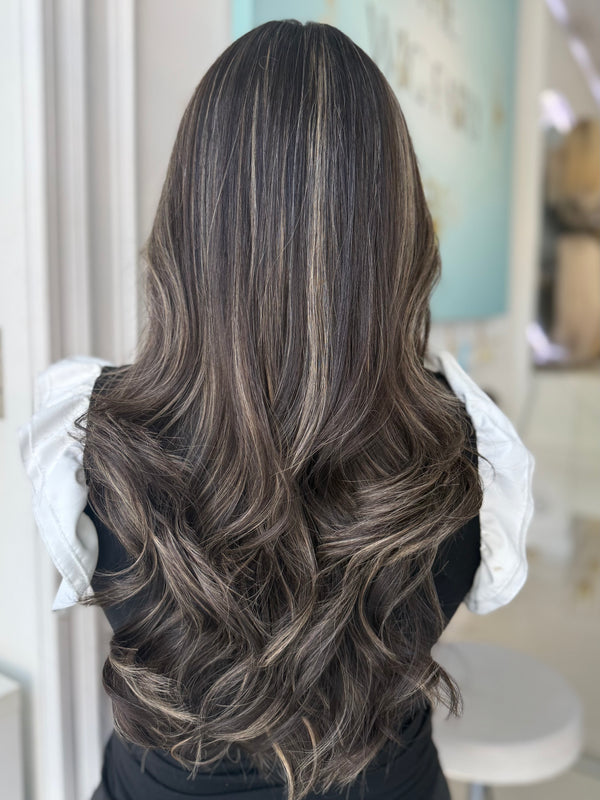 Ivy skin top wig, 24 inches in dark brown with light brown highlights, with pre-cut lace for a flawless, natural look, styled in elegant waves.
