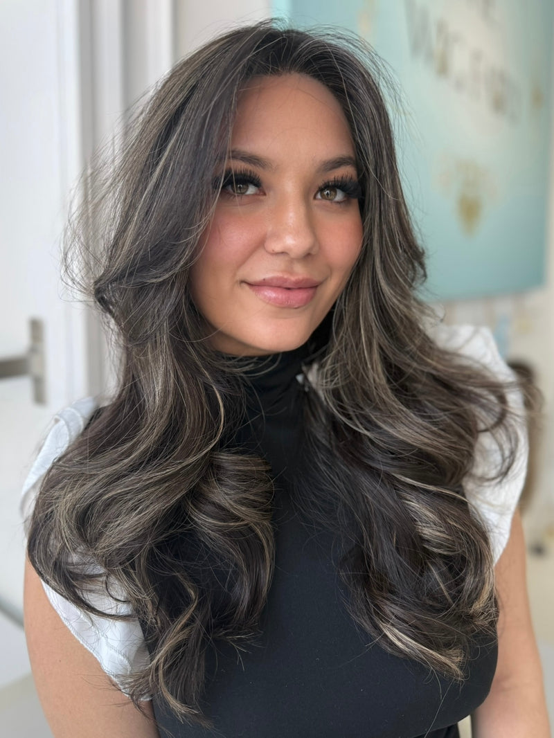 Ivy wig with a skin top, 24-inch length in dark brown with light brown highlights, styled in soft waves for a glamorous, natural look with pre-cut lace for easy wear.
